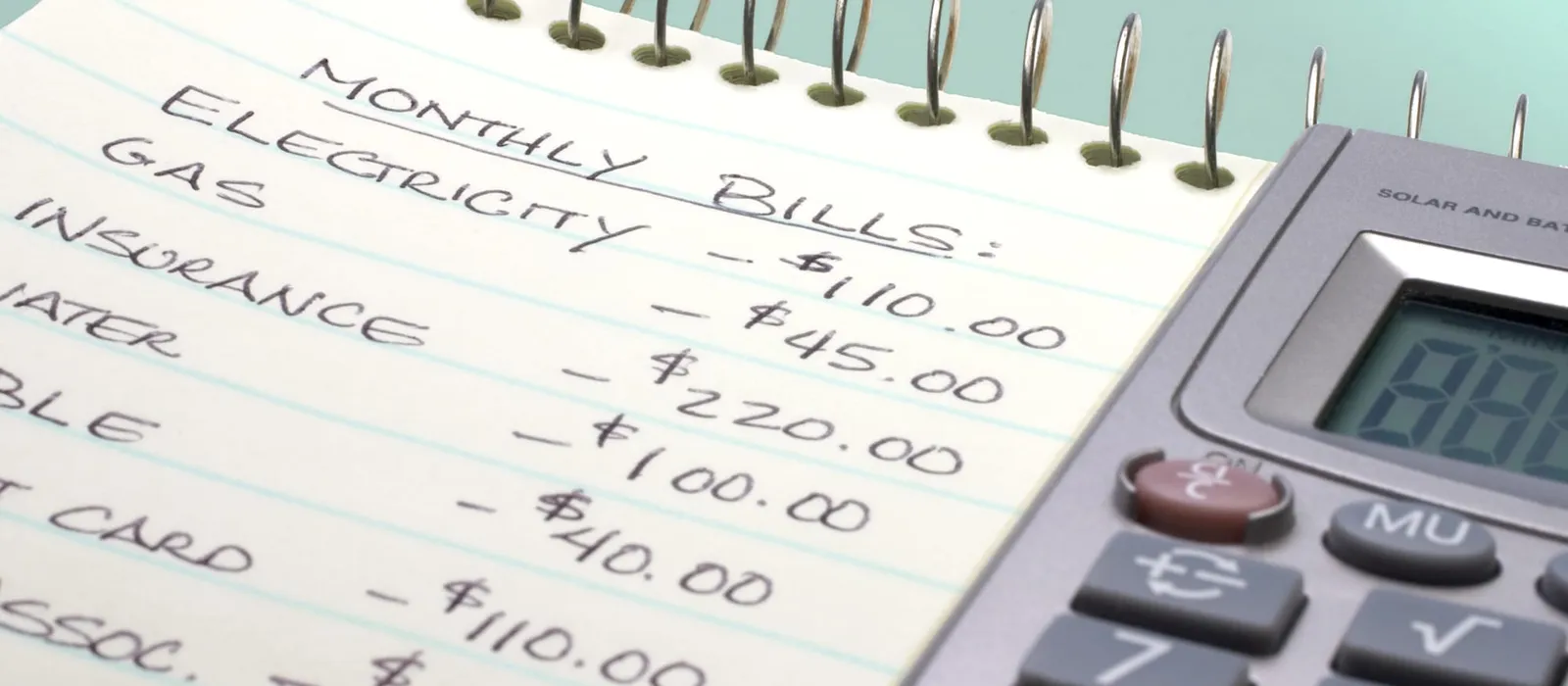 Monthly bills summed on a notepad beside a calculator