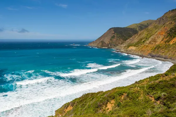 Surf rolling into a cove below green hills