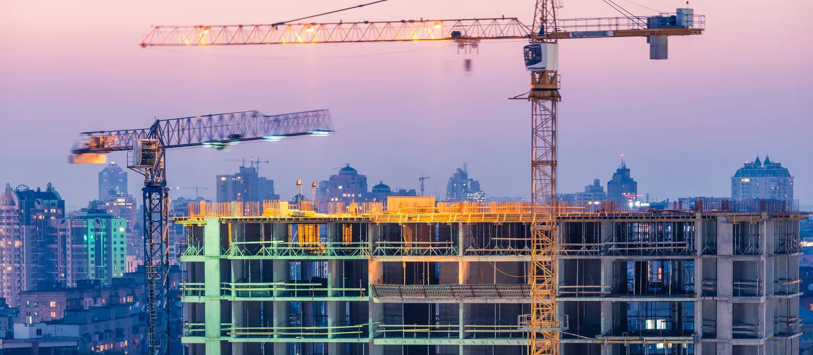 Office building under construction with two cranes at sunset