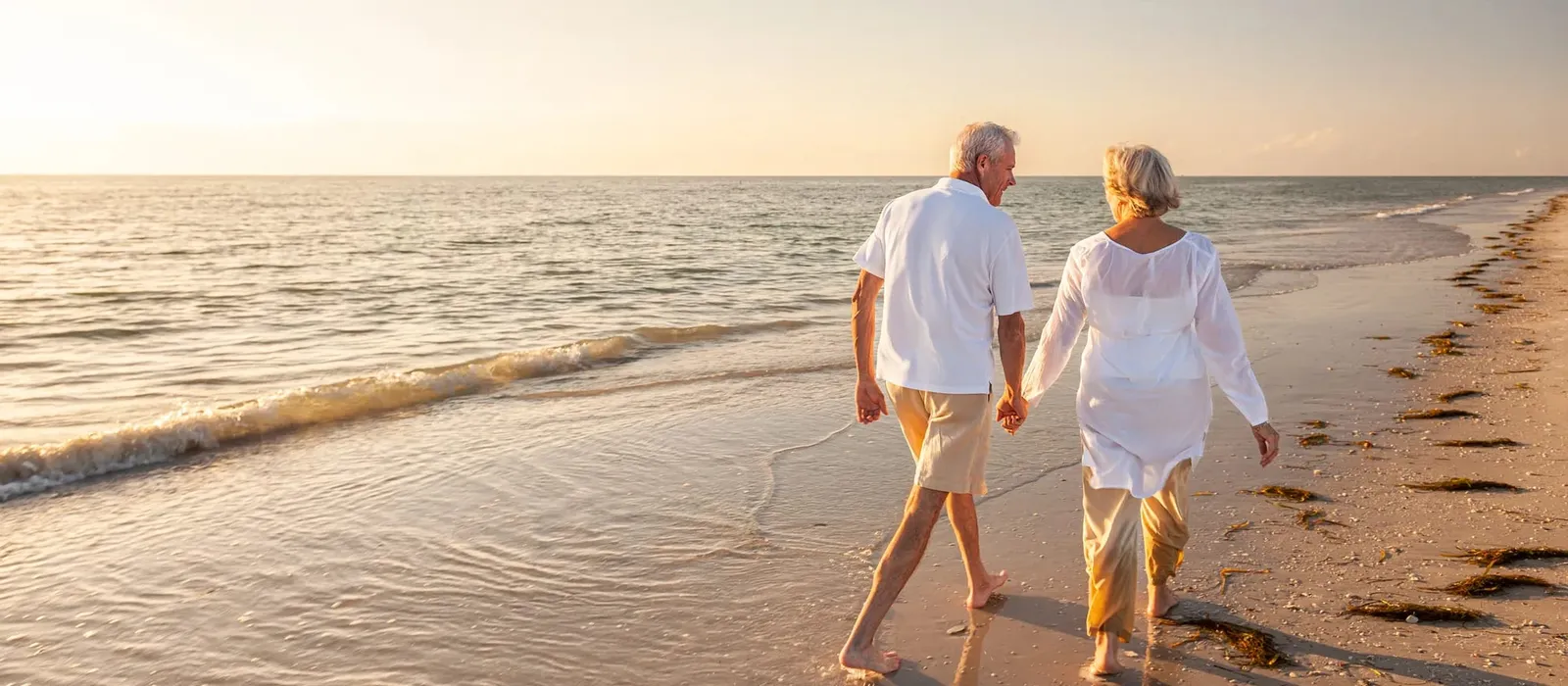Retired couple walking hand in hand on a beach at sunset